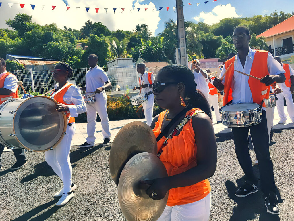 Fanfare des Viducasses en plein défilé en Guadeloupe, avec la présidente au premier plan tenant des cymbales et les musiciens derrière elle.