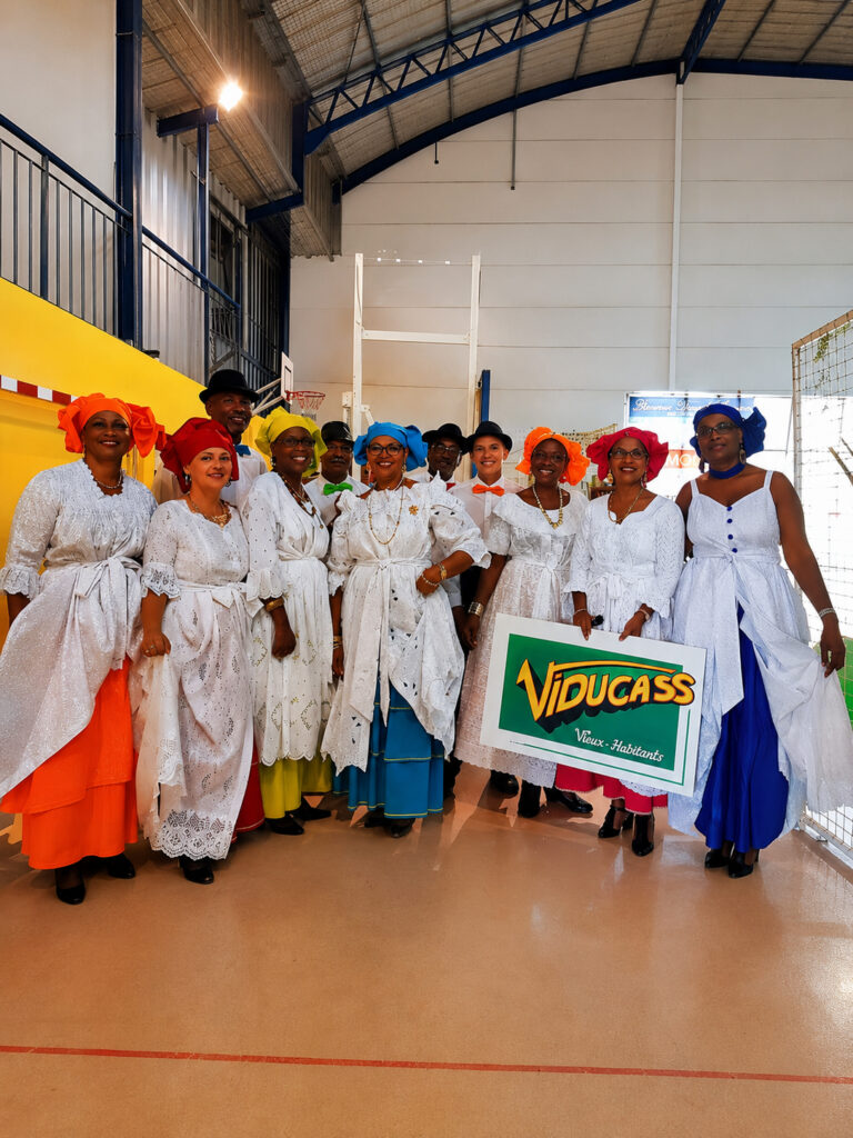Groupe de quadrille des Viducasses en tenue traditionnelle créole avec robes blanches, maré tèt colorés et pancarte de l’association